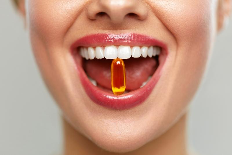 Woman smiling with vitamin between her teeth